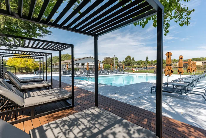 Inviting outdoor pool area with stylish pergolas, comfortable lounge chairs, and chic umbrellas under a vibrant blue sky.