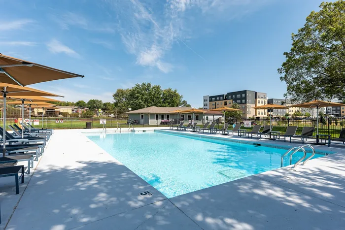 Luxurious outdoor pool area with sleek lounge chairs and modern umbrellas, surrounded by lush greenery and contemporary buildings.