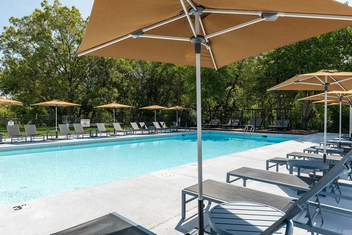 Inviting outdoor pool area with elegant lounge chairs and stylish umbrellas, surrounded by lush greenery.