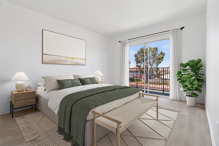 Bright and airy bedroom with elegant decor featuring a large bed, modern artwork, and a cozy bench. Floor-to-ceiling windows open to a scenic balcony, while a lush indoor plant adds a touch of nature.
