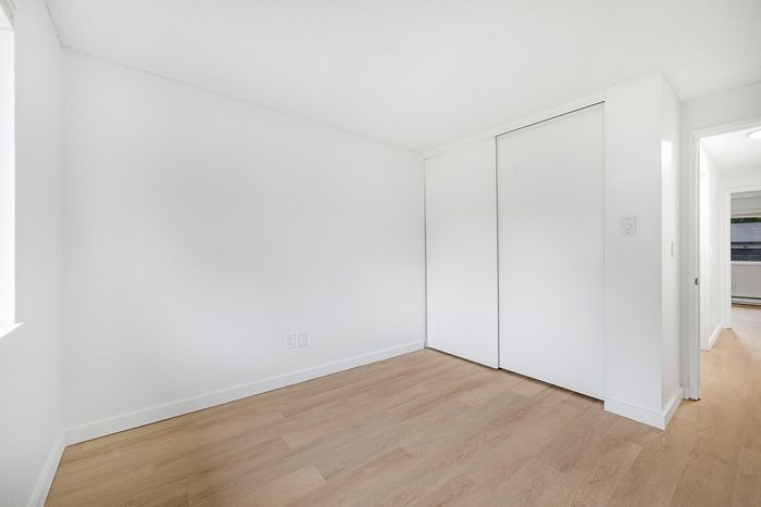 Bright bedroom with sleek wooden floors and ample closet space, showcasing modern minimalist charm.