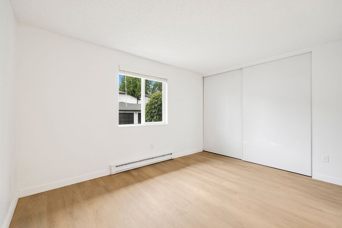 Bright, airy bedroom with large window, sleek wooden floors, and modern white sliding closet doors.