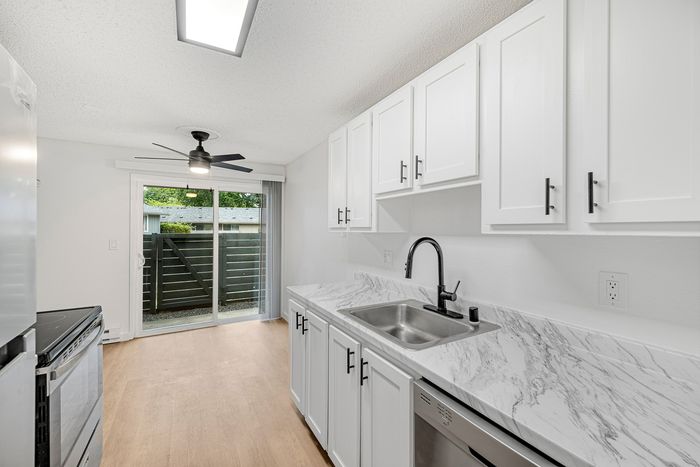 Modern kitchen with sleek white cabinetry, marble countertops, stylish black fixtures, and natural light from sliding glass doors leading to a private patio.