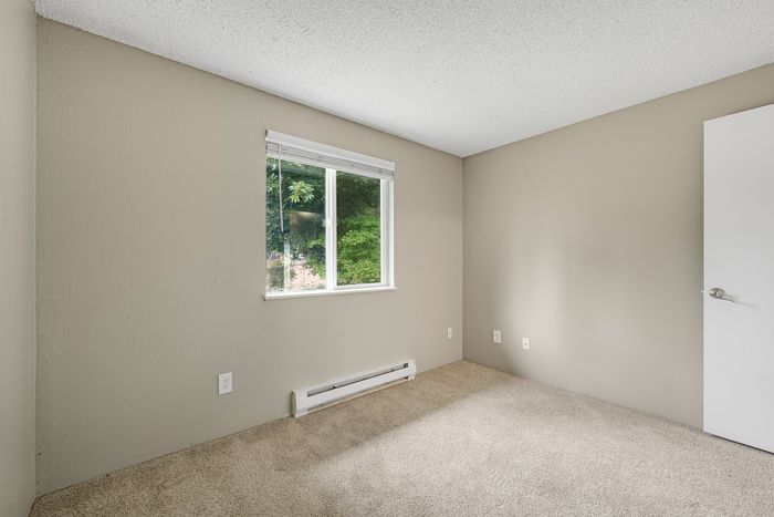Bright, neutral-toned bedroom with plush carpet and a large window offering scenic green views.