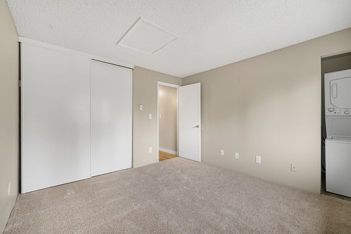 Inviting bedroom with plush carpet flooring, white sliding closet doors, and in-unit laundry for modern convenience.