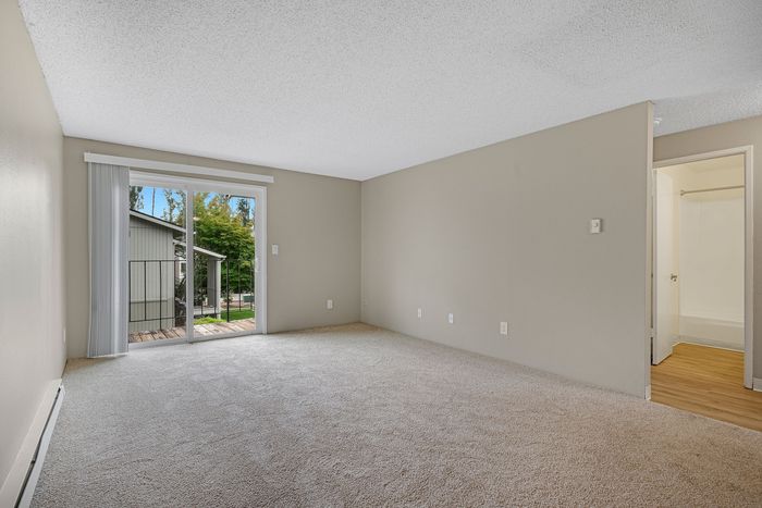 Bright, spacious living room featuring plush carpeting, a large sliding glass door leading to a balcony, and a connected bathroom with modern amenities.