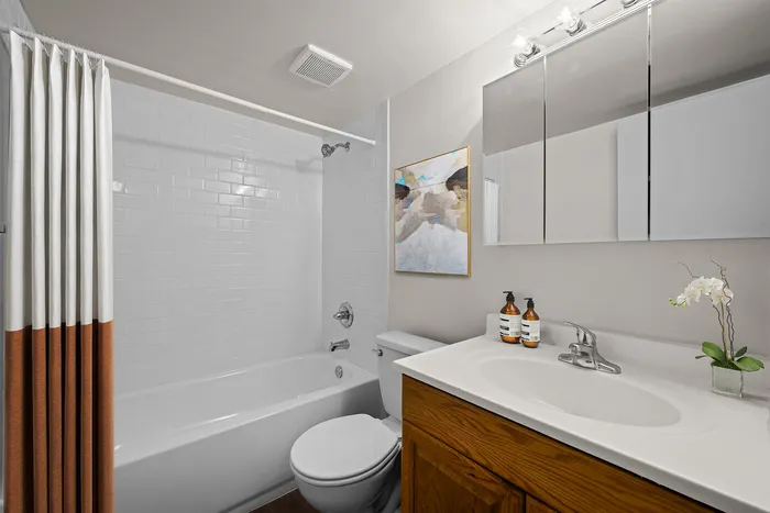 Modern bathroom with sleek white tiles, stylish wooden vanity, elegant mirror, and a relaxing bathtub.