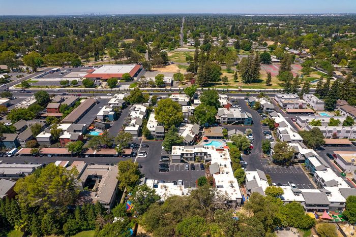 Vibrant aerial view of a spacious apartment community surrounded by lush greenery, featuring a central swimming pool and ample parking.