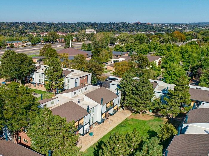 Scenic aerial view of a lush green residential area with modern apartment buildings surrounded by trees and a wide road nearby.