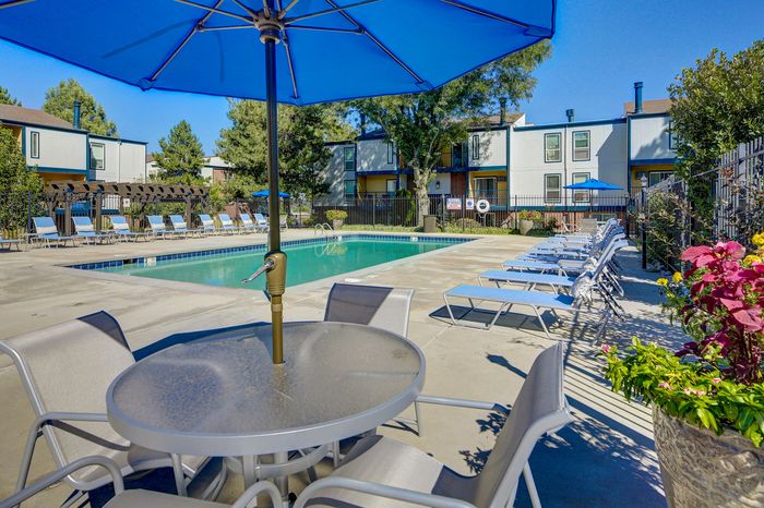Inviting pool area with comfortable lounge chairs and shaded seating, surrounded by lush greenery and charming buildings.