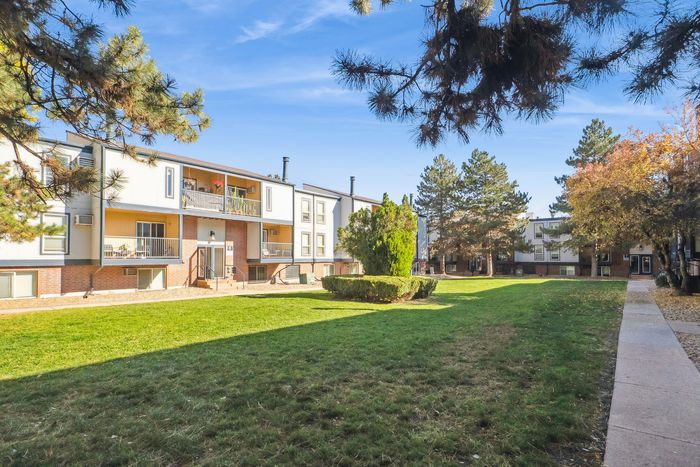 Charming residential building with spacious balconies overlooking a lush, green courtyard, surrounded by mature trees under a clear blue sky.