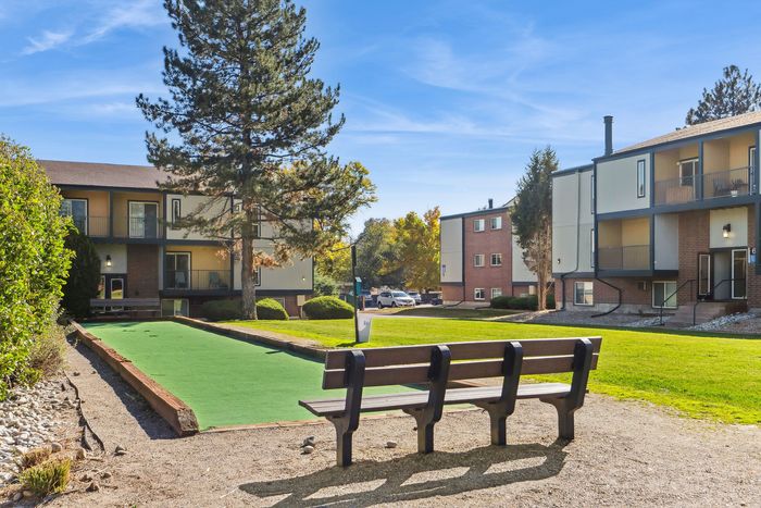 Charming apartment complex with spacious balconies, lush greenery, and recreational bocce court under a clear blue sky.
