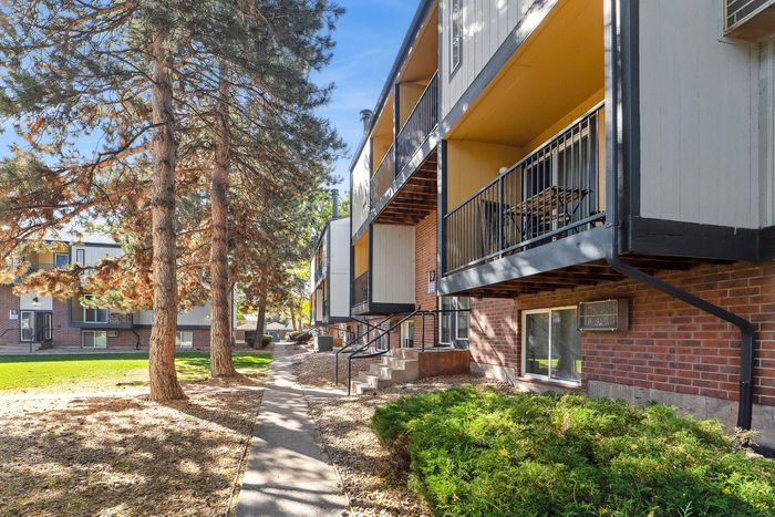 Charming apartment building exterior with spacious balconies surrounded by lush greenery and tall trees, offering serene living.