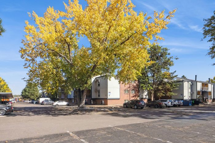 Inviting apartment complex with spacious parking, surrounded by vibrant autumn foliage and clear blue skies.