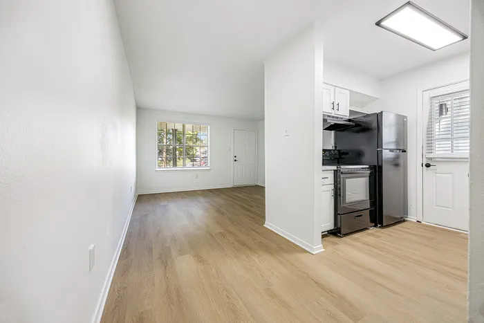 Bright and airy apartment with open living space, modern kitchen featuring sleek black appliances, and elegant wood flooring.