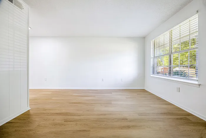 Bright and airy room with sleek wooden floors, large window, and calming white walls, offering a serene living space.