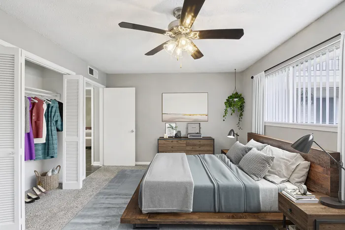 Inviting bedroom with elegant ceiling fan, cozy blue bedding, modern wooden furniture, and ample natural light from large windows.