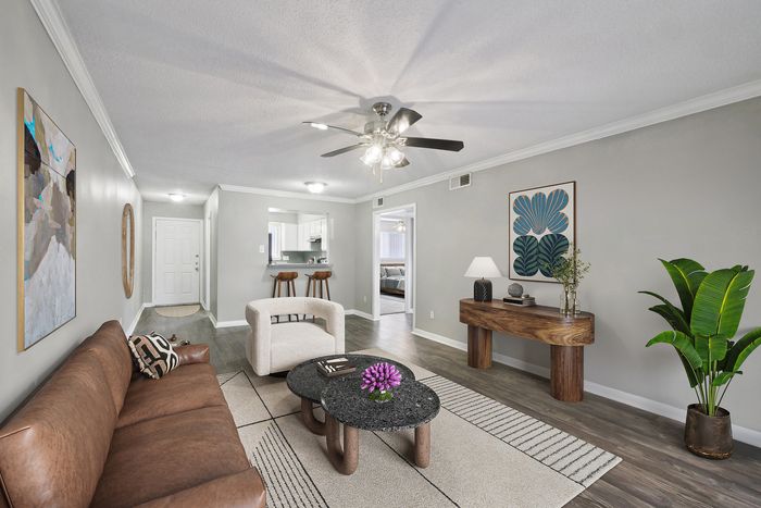 Elegant living area with chic decor and stylish furniture, bright open layout, cozy sofa, modern coffee table, and vibrant plant accents. Inviting kitchen view with bar stools, ideal for entertaining.
