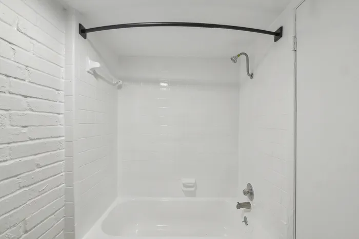 Modern bathroom featuring a pristine white tiled shower and bath combo with sleek fixtures.