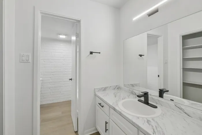 Sleek modern bathroom with marble countertop, elegant white cabinetry, and spacious mirror for a bright and stylish ambiance.