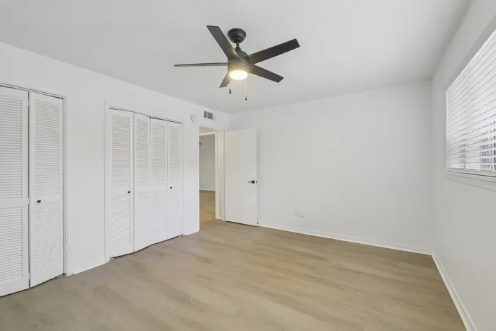 Bright and airy bedroom featuring sleek wooden floors, a modern ceiling fan, and ample closet space.