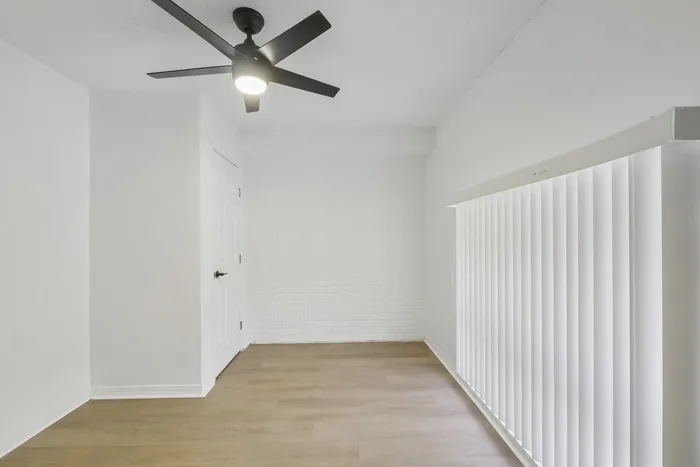 Bright, modern room featuring sleek ceiling fan, textured white brick wall, and elegant vertical blinds.