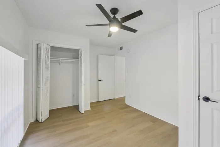 Bright and airy bedroom with sleek light wood flooring, a modern ceiling fan, and ample closet space.