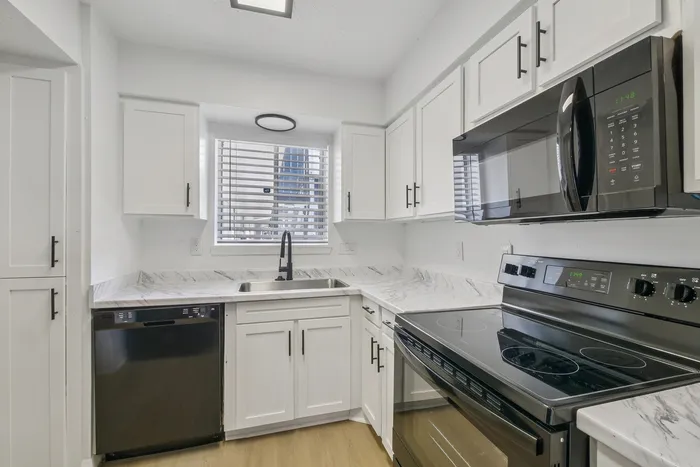 Modern kitchen with sleek black appliances, white cabinetry, and elegant marble countertops.
