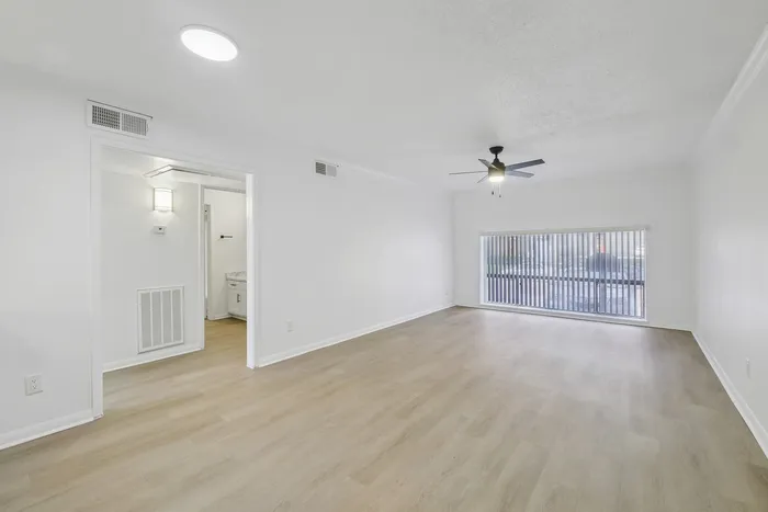 Spacious modern apartment with sleek wood flooring, large window offering natural light, and a stylish ceiling fan.