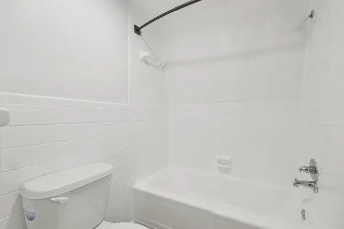 Bright and modern bathroom featuring a pristine white bathtub, sleek fixtures, and a stylish tile finish, perfect for relaxing and unwinding.