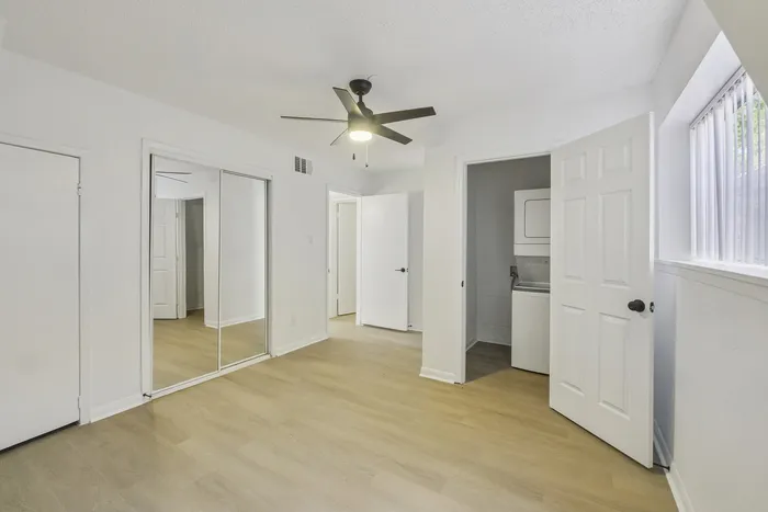 Bright and spacious room with elegant mirrored closet doors, modern ceiling fan, and convenient in-unit laundry.