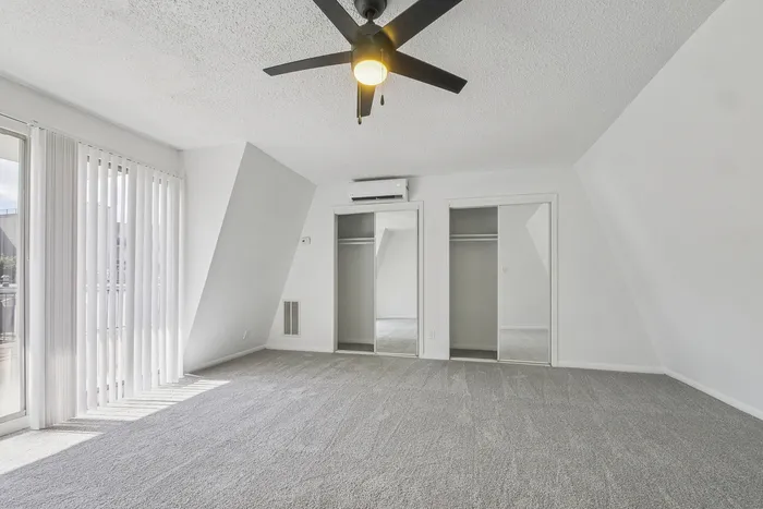 Bright and spacious bedroom with modern ceiling fan, mirrored closets, and large sliding window doors leading to a private balcony.
