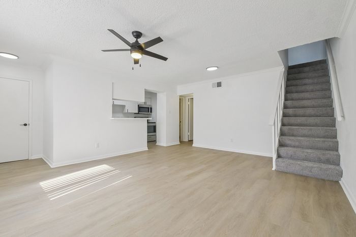 Inviting open-concept living space with sleek laminate flooring, modern ceiling fan, and carpeted staircase leading to the upper level.