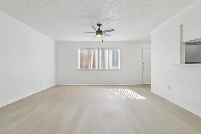 Bright and spacious living area with elegant light wood flooring and modern ceiling fan, inviting natural light through large windows.