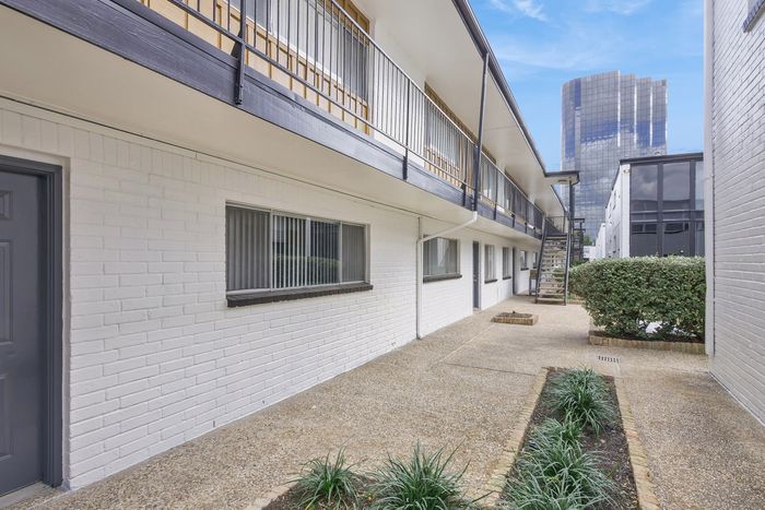 Chic urban apartment exterior with a modern white brick facade, lush greenery, and a striking cityscape backdrop.