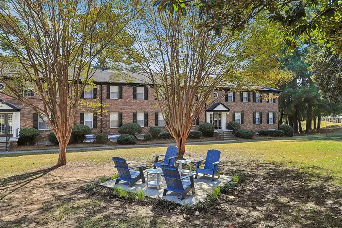 Charming brick apartment complex with serene outdoor seating area surrounded by lush greenery.