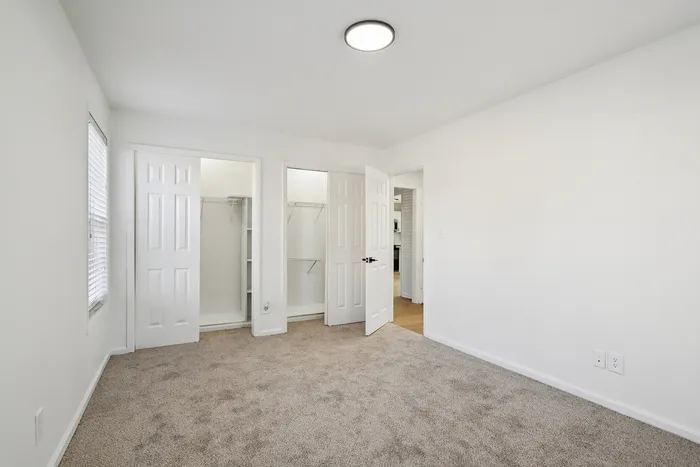 Bright, airy bedroom with plush carpeting, dual closets, and crisp white walls offering modern comfort.