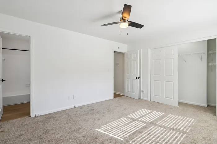 Spacious bedroom with plush carpeting, ample natural light, and a modern ceiling fan in a stylish apartment.