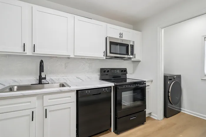 Modern kitchen with sleek black appliances and elegant white cabinetry, featuring a marble countertop and stylish black fixtures.