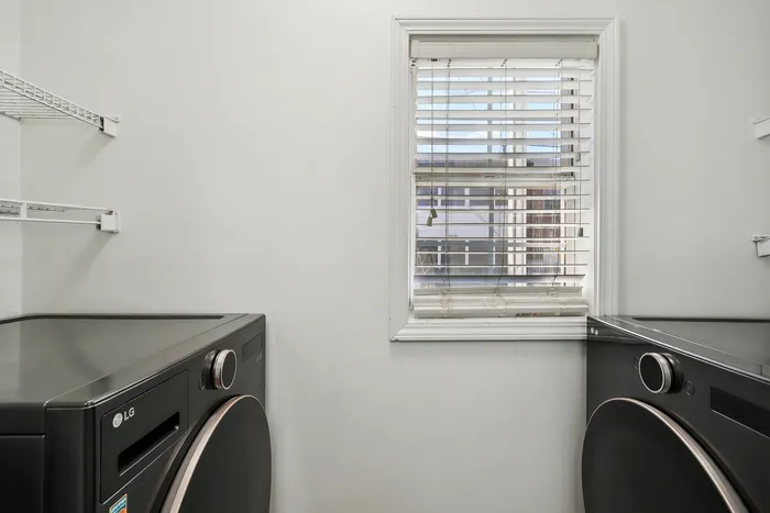Modern laundry room with sleek black appliances, bright window lighting, and efficient shelving.