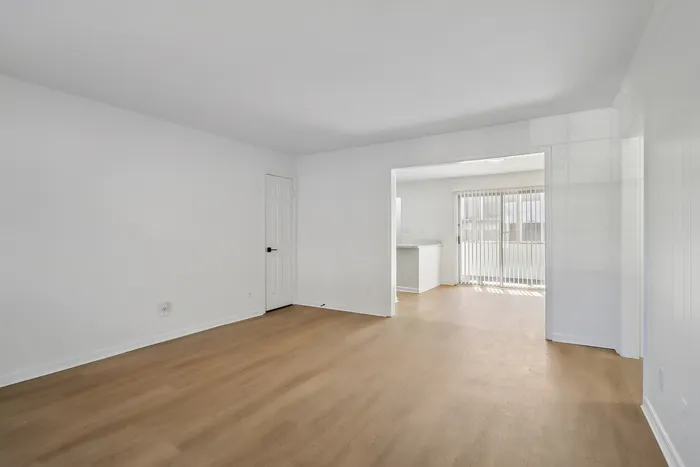 Bright and airy living space with elegant wood flooring, leading to a sunlit room through sliding glass doors.