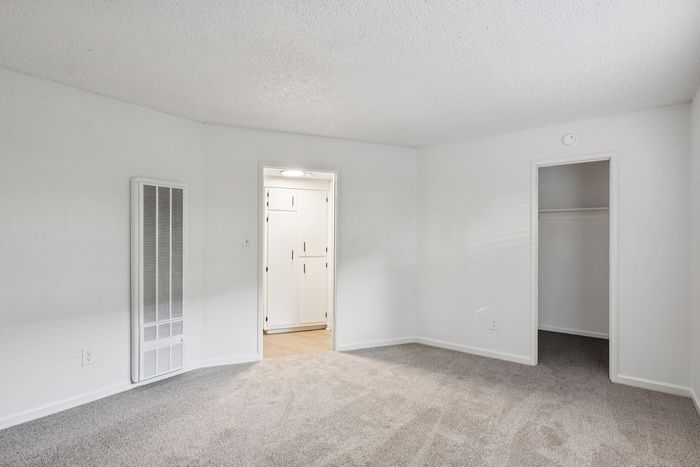 Bright room with plush carpet and white walls leading to a cozy kitchen area, featuring ample storage space and a walk-in closet.