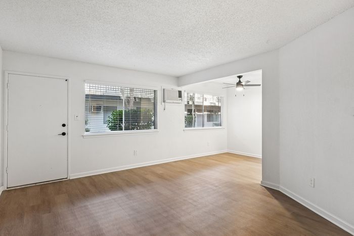 Bright and inviting living area with hardwood floors, large windows, and modern ceiling fan, perfect for cozy gatherings.