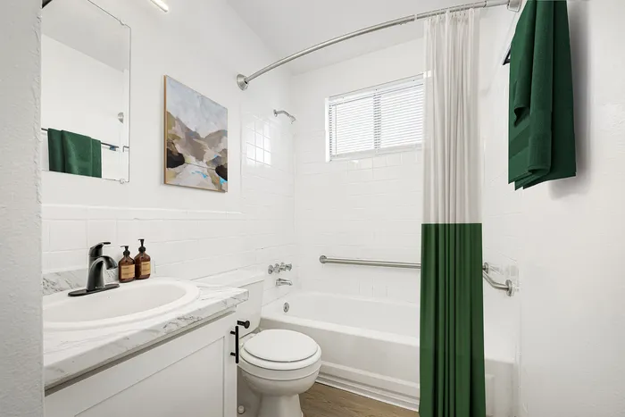 Bright and modern bathroom featuring a white tiled bathtub, sleek marble countertop sink, and elegant green accents.