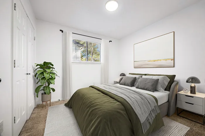 Modern bedroom with stylish green bedding, chic bedside tables, and bright natural light through large window, featuring elegant plant decor.