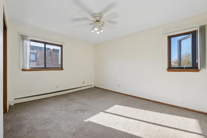 Bright and airy room featuring large windows, fresh carpet, and a ceiling fan, perfect for comfort and relaxation.