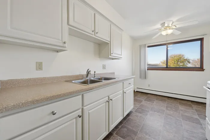 Bright and modern kitchen with sleek white cabinets, spacious countertops, and a large window offering scenic views.