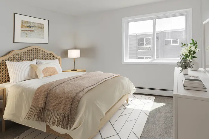 Cozy and bright bedroom featuring a luxurious bed with a woven headboard, elegant lamp, and a large window with a tranquil view.