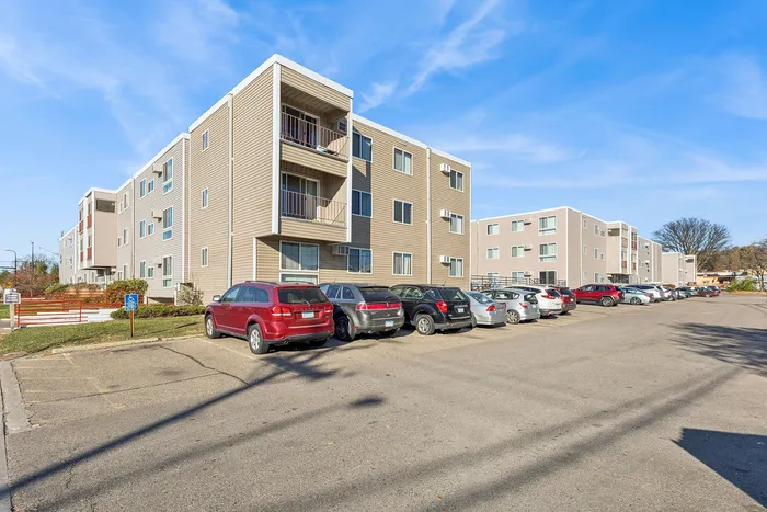 Modern apartment complex with stylish exterior architecture, ample parking, and wide open sky backdrop on a sunny day.