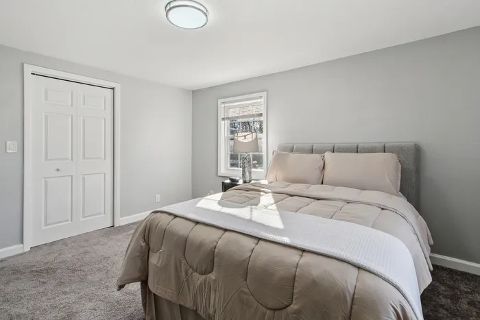 Inviting bedroom featuring a plush bed with neutral bedding, natural light from a large window, and modern decor for a serene atmosphere.